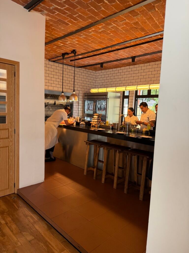 El zaguán que no anuncia nada Cocina abierta de Atte. con el equipo trabajando, techo de ladrillo aparente